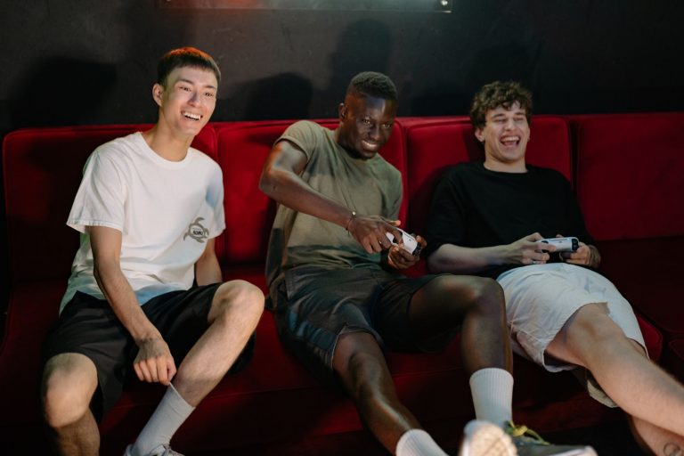 Three diverse young men sitting on a red couch, enjoying a fun video game session together. — Exclusive Access: High Roller G