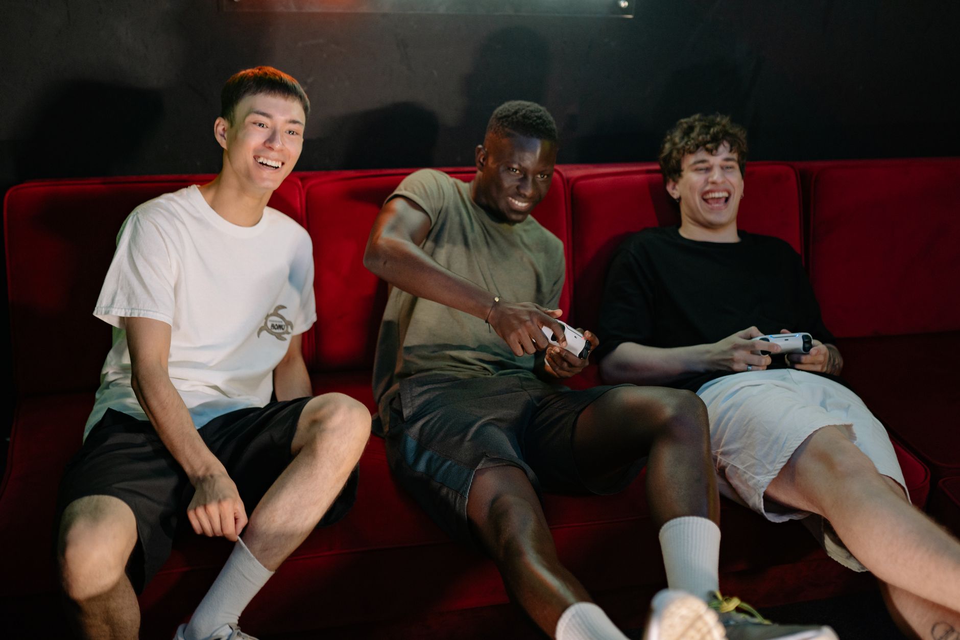 Three diverse young men sitting on a red couch, enjoying a fun video game session together. — Exclusive Access: High Roller G