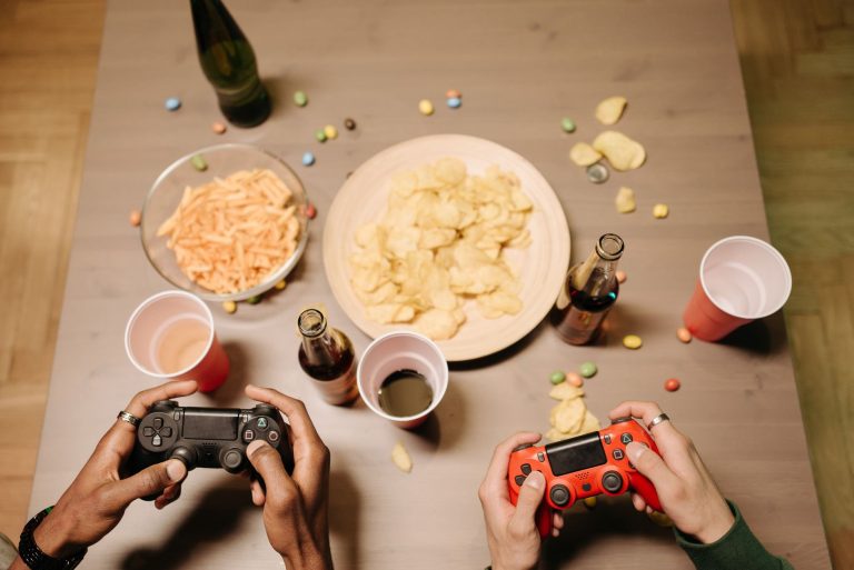 Two gamers playing video games with snacks and drinks on table, a perfect setup for gaming night. — UFA656 Online Casino Serv